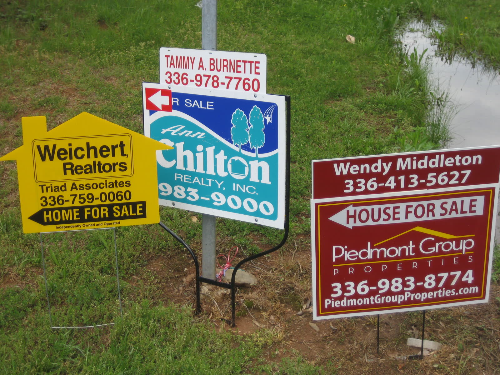 A for-sale sign standing in front of houses.
