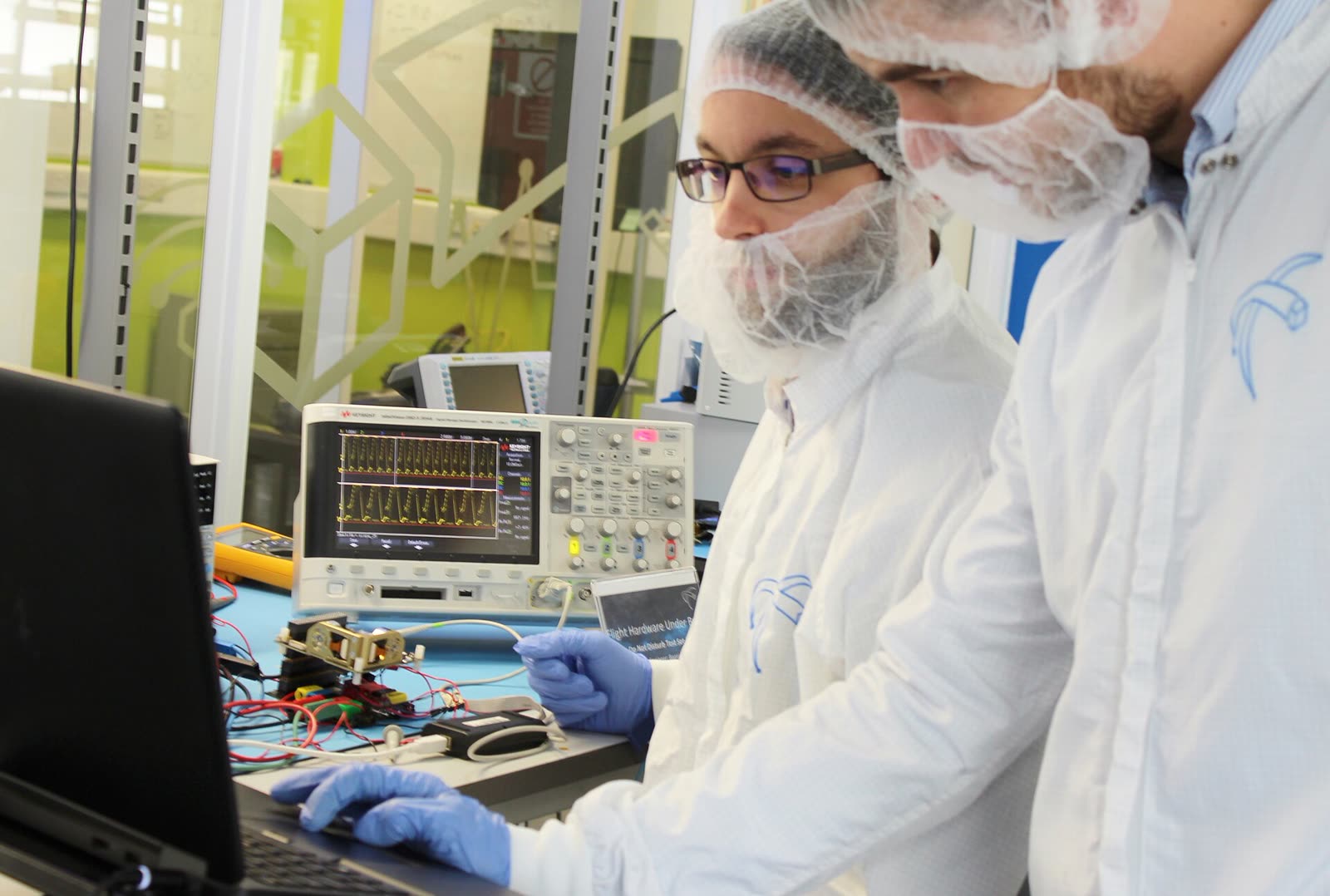 Photograph of two cleanroom engineers working with electronic test equipment in a laboratory.