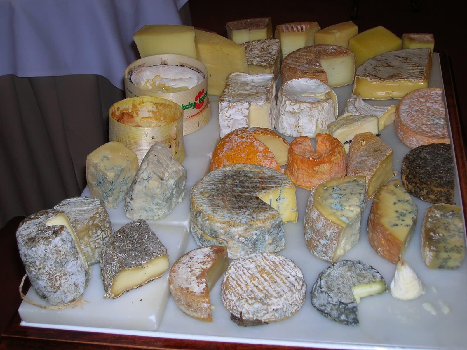 A cheese trolley with multiple whole and cut cheeses in a fine-dining restaurant.