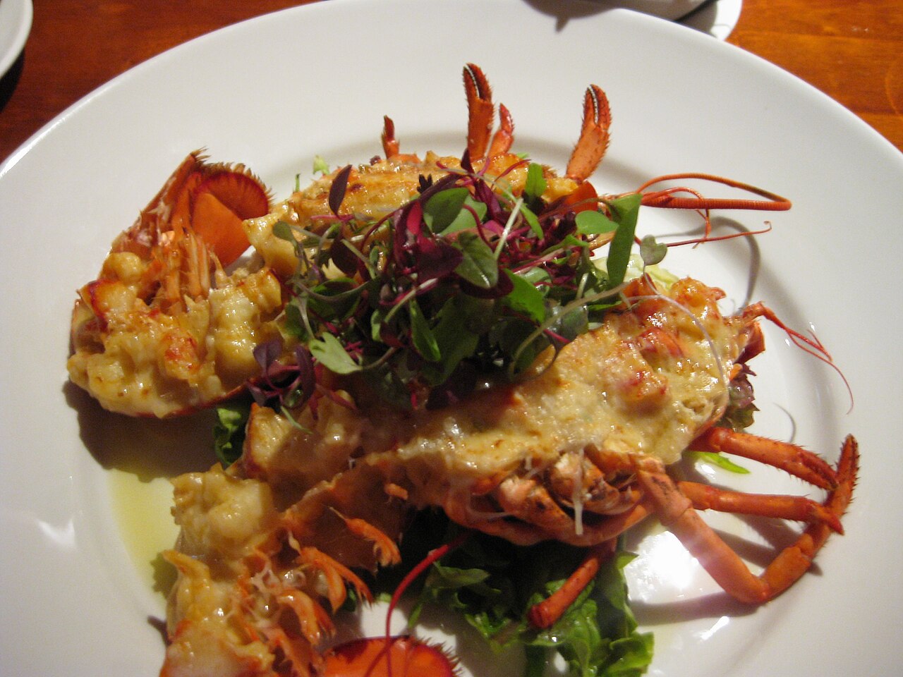 A serving of Lobster Thermidor in a lobster shell with browned sauce and garnish on a restaurant plate.