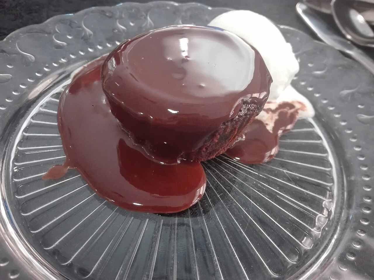 A chocolate coulant cut open on a white plate, with molten chocolate flowing from the center.