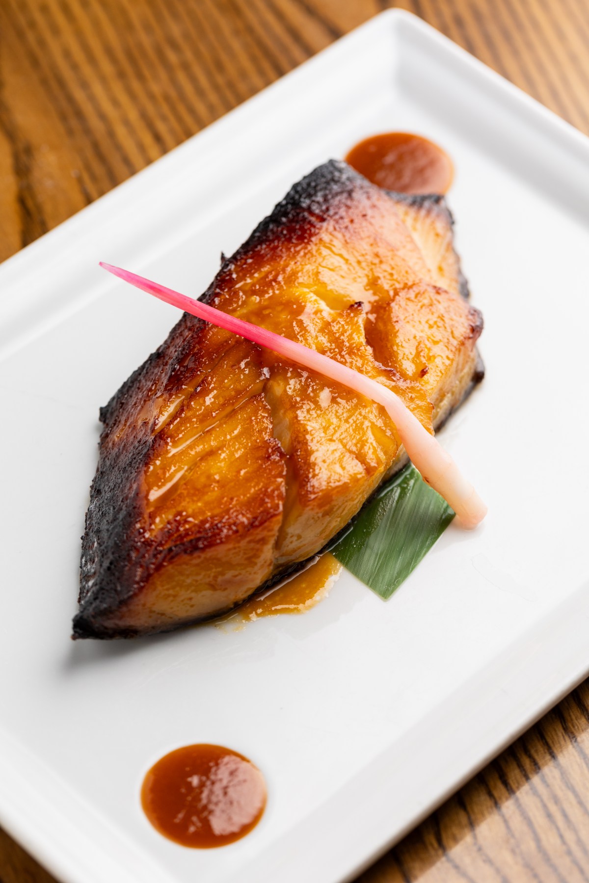 Nobu 的味噌腌黑鳕鱼盛在白盘中，旁边有酱汁圆点和一小块腌姜。