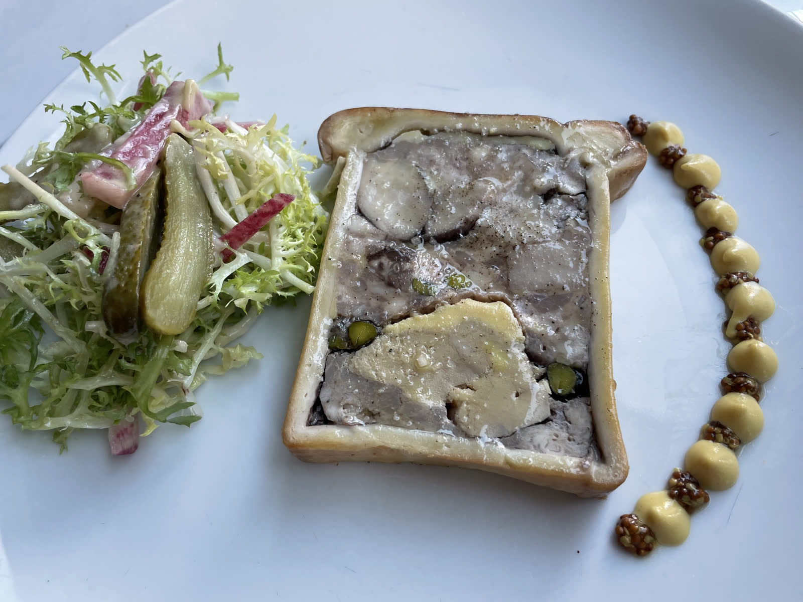 A sliced pate en croute showing a dark forcemeat center, pastry crust, and a line of jelly on a white plate.