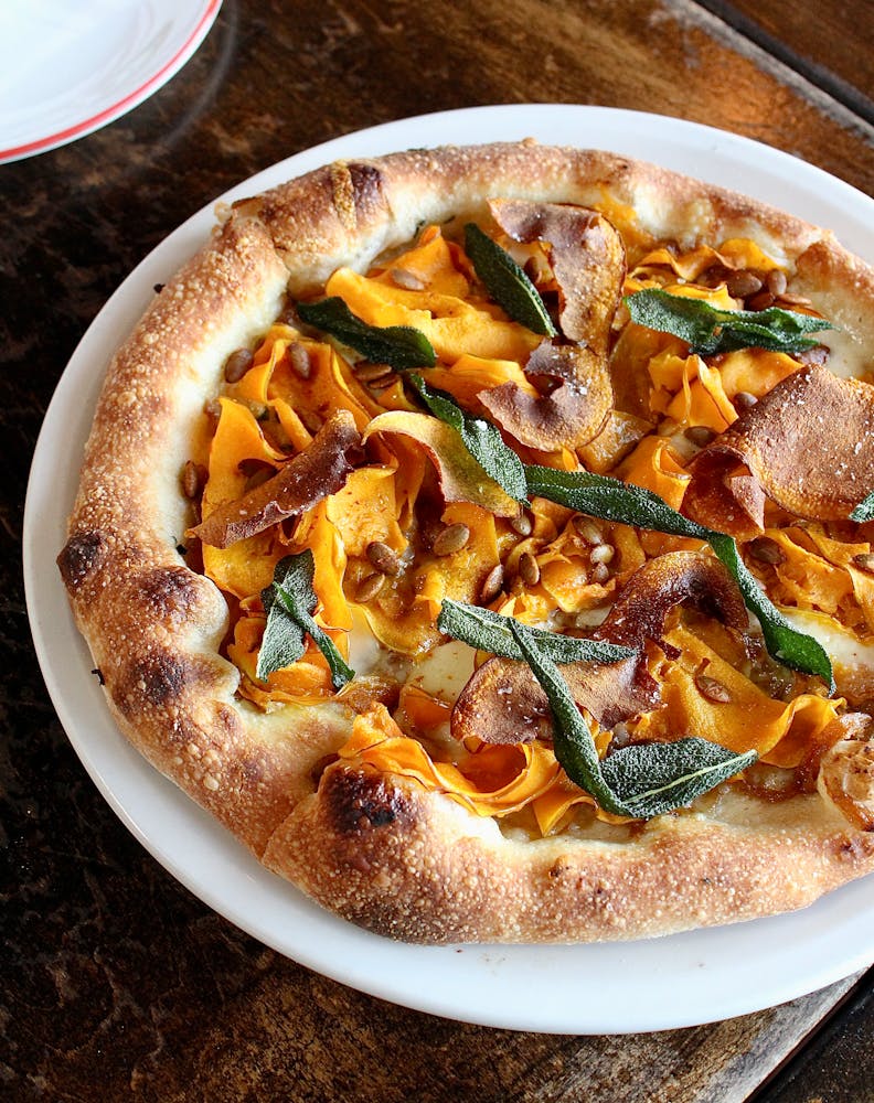 A close-up official photograph of a Pizzeria Mozza pizza with vegetables and cheese on a browned crust.