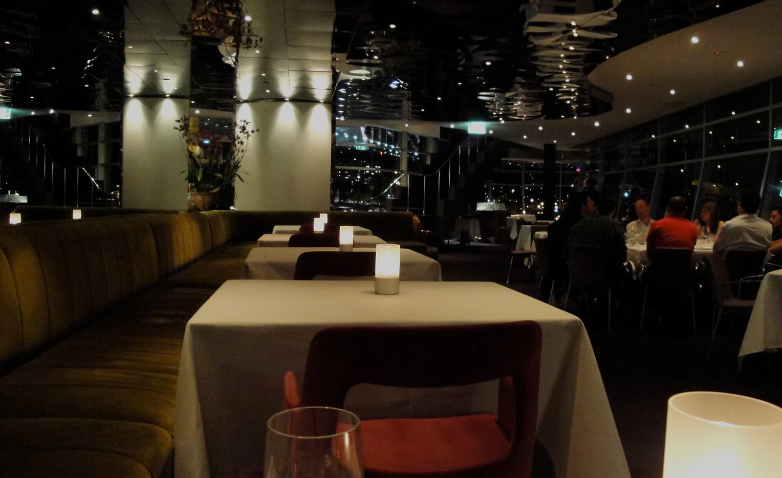一张悉尼 Quay 餐厅 dining room 的真实照片，画面中有摆好的餐桌、玻璃杯，以及面向海港的窗。