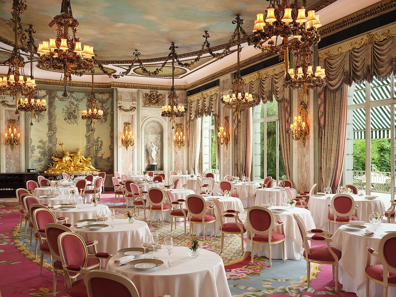 伦敦The Ritz Restaurant餐室，圆形白桌布餐桌、红色餐椅、高窗、枝形吊灯和鎏金墙面装饰清晰可见。