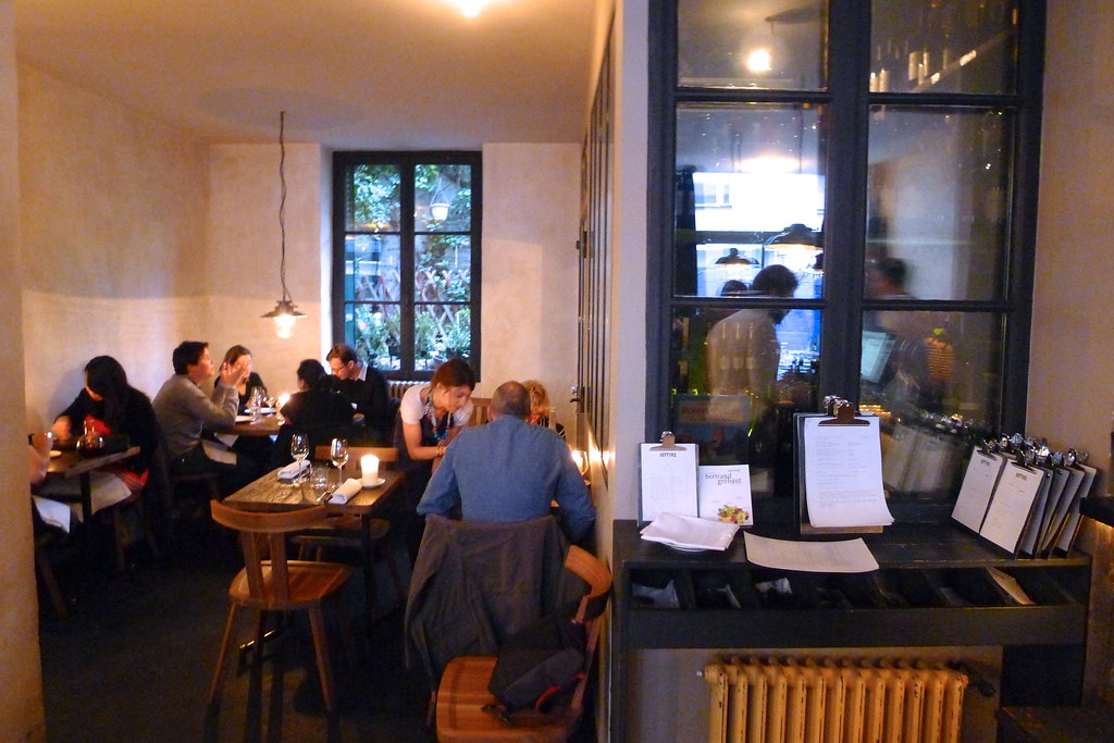 The interior of Restaurant Septime in Paris, with small wooden tables, seated diners, candlelit settings, and warm bistro lighting.