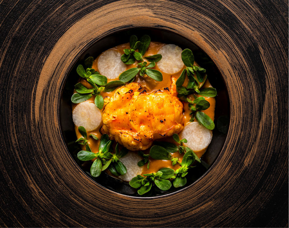 A plated Sublime dish photographed from above, with a golden central piece, green leaves, pale rounds, and a dark circular plate.