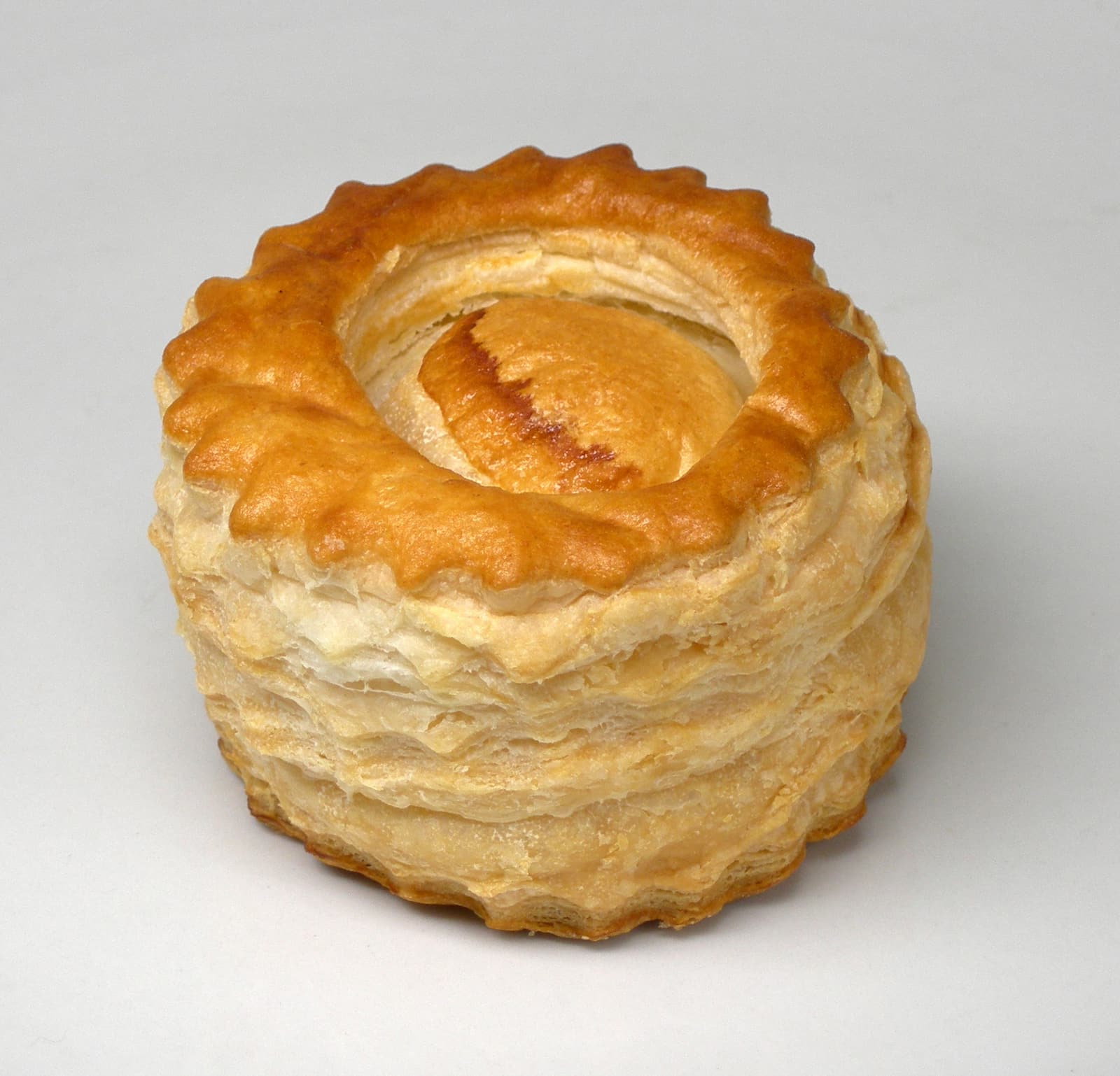 A photographed vol-au-vent with a golden puff pastry shell filled with creamy savory ragout on a white plate.