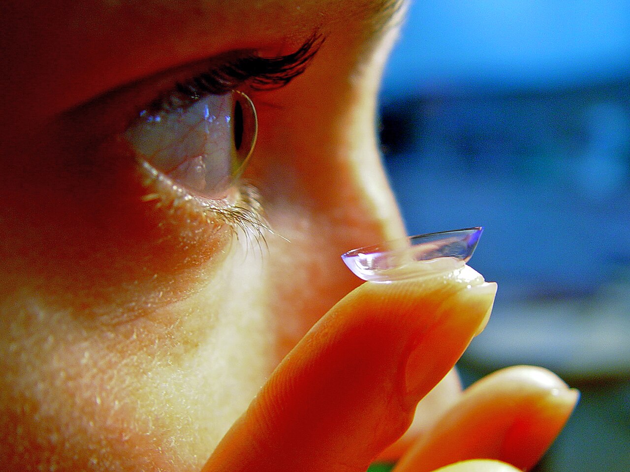 Photograph of a person holding a soft contact lens on a fingertip near one eye.