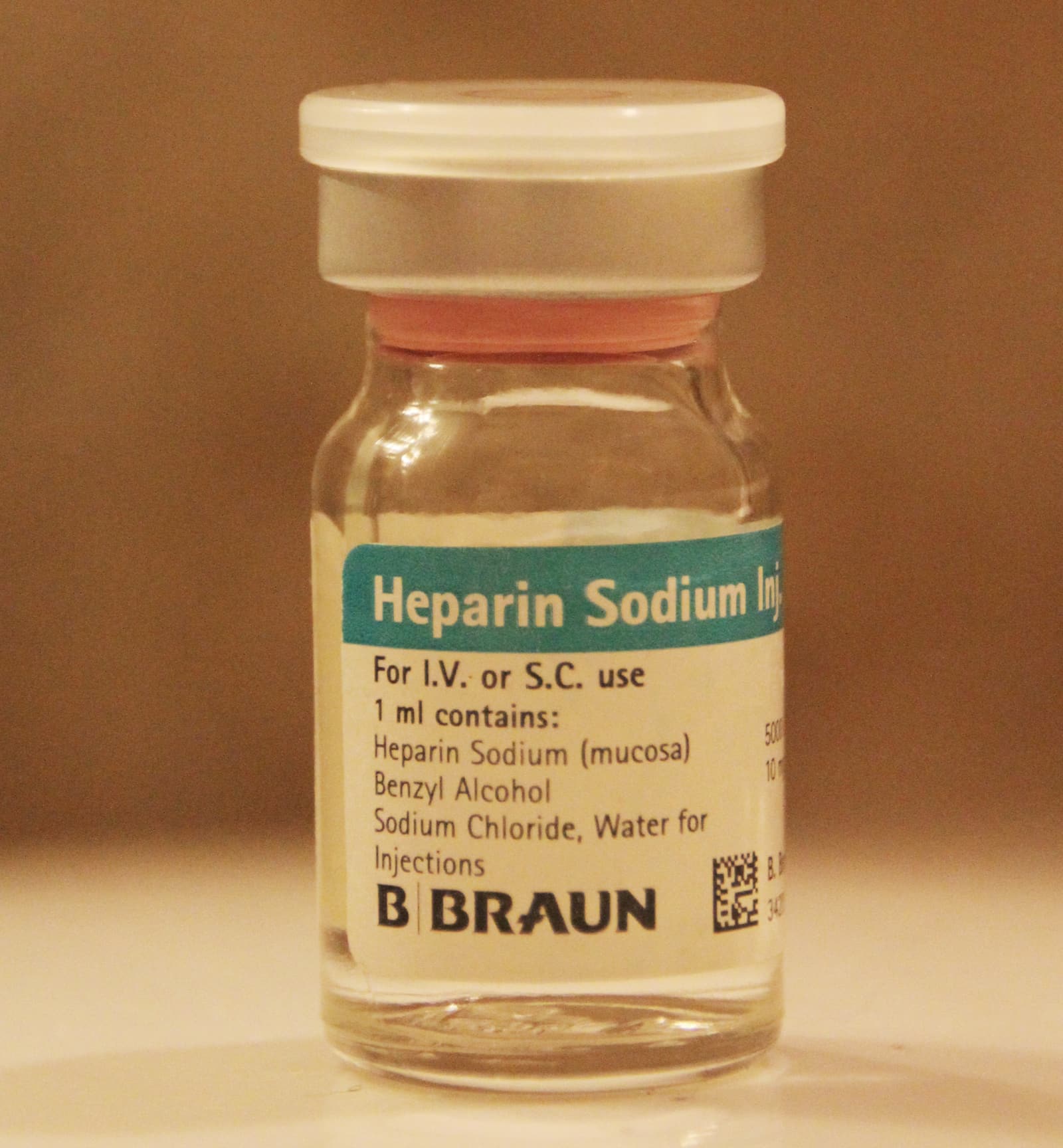 一只透明玻璃小瓶的照片，标签写有 Heparin Sodium Injection，瓶盖为白色，标签为青绿色。