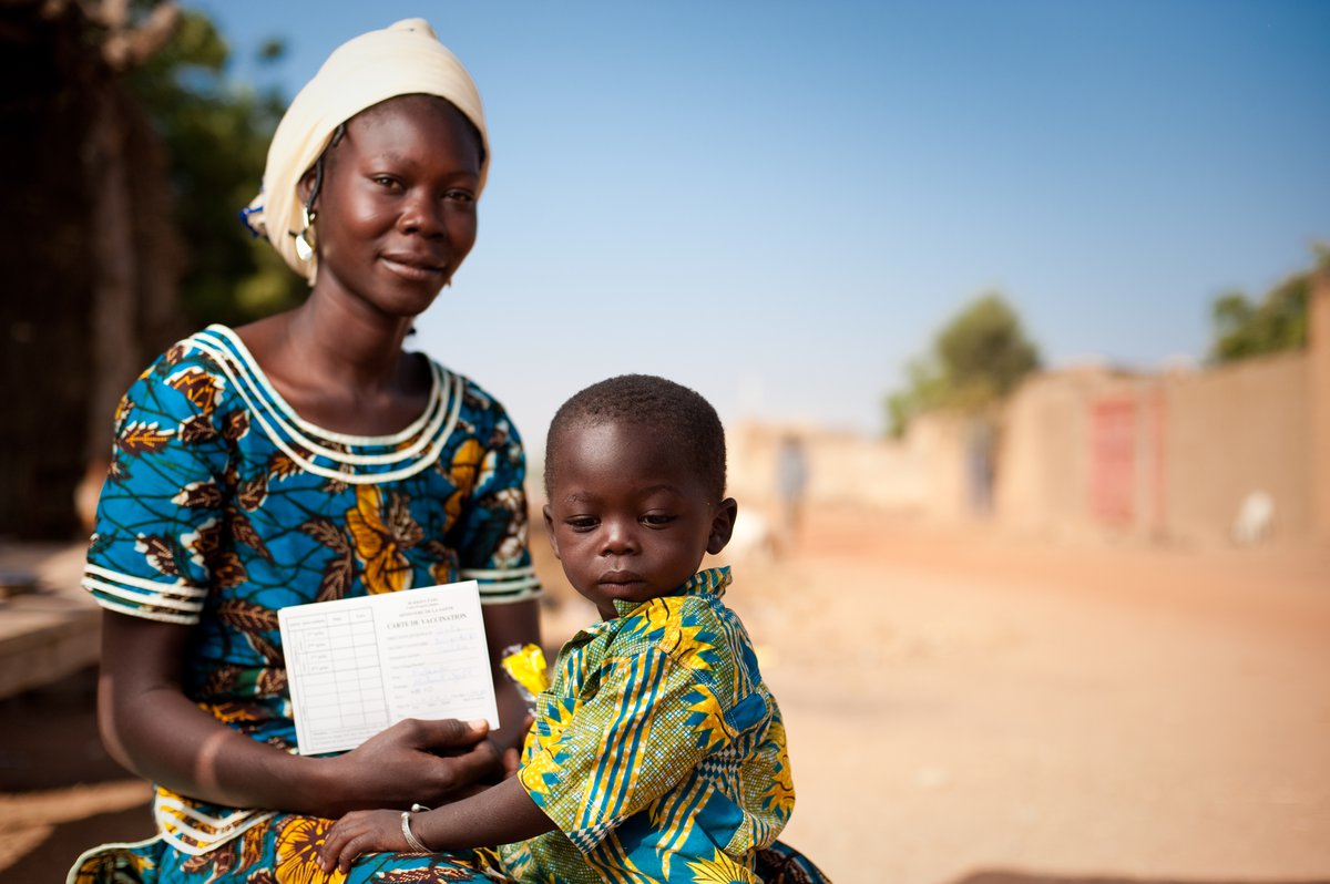 A mother in Burkina Faso holding a child and displaying the child's MenAfriVac vaccination record.