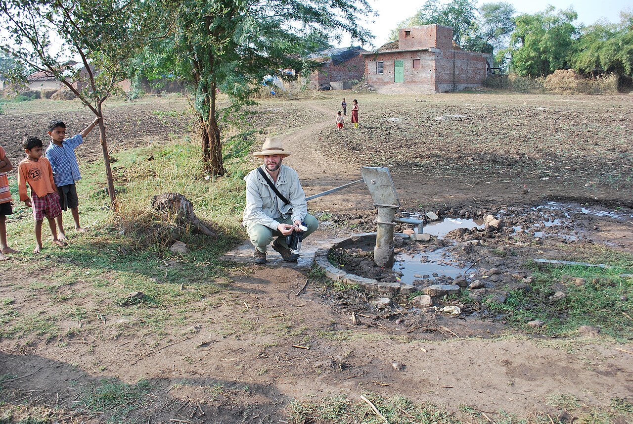 Photograph of a researcher kneeling beside a hand well while testing drinking-water samples in rural Gujarat.