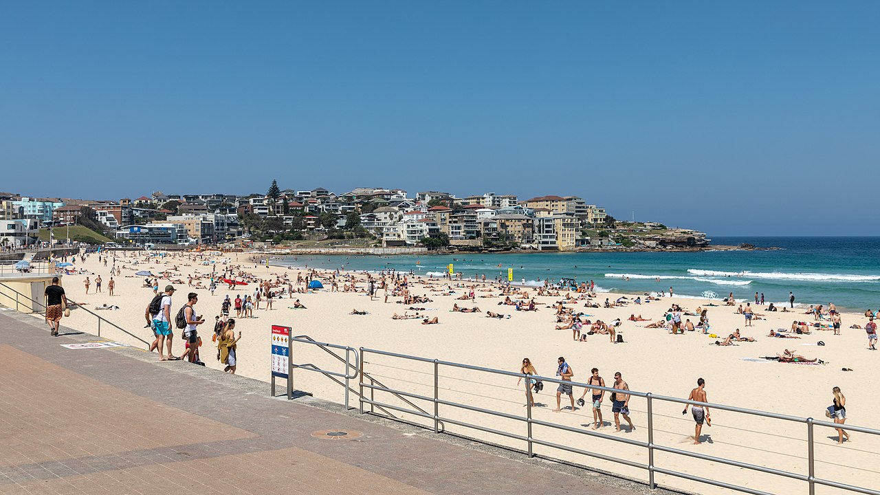 Photograph of Bondi Beach in Sydney on a sunny day, with beachgoers, sand, surf, and the coastal backdrop.