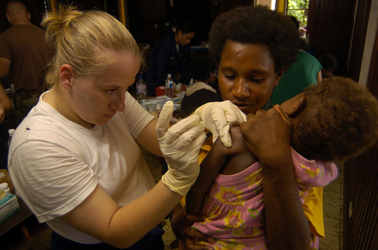 A U.S. Navy hospital corpsman administers a tetanus shot to a child held by her mother.