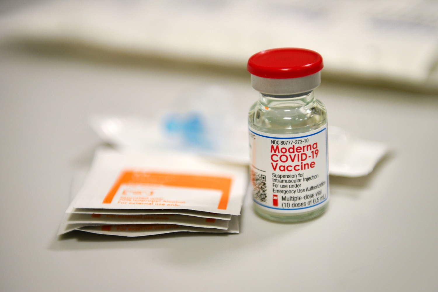 Photograph of a vaccine vial held upright by a gloved hand.