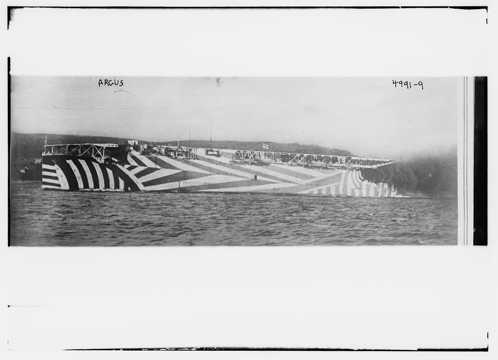 Archival photograph of HMS Argus in high-contrast dazzle camouflage, with angular black and white paint bands disrupting the ship's profile.