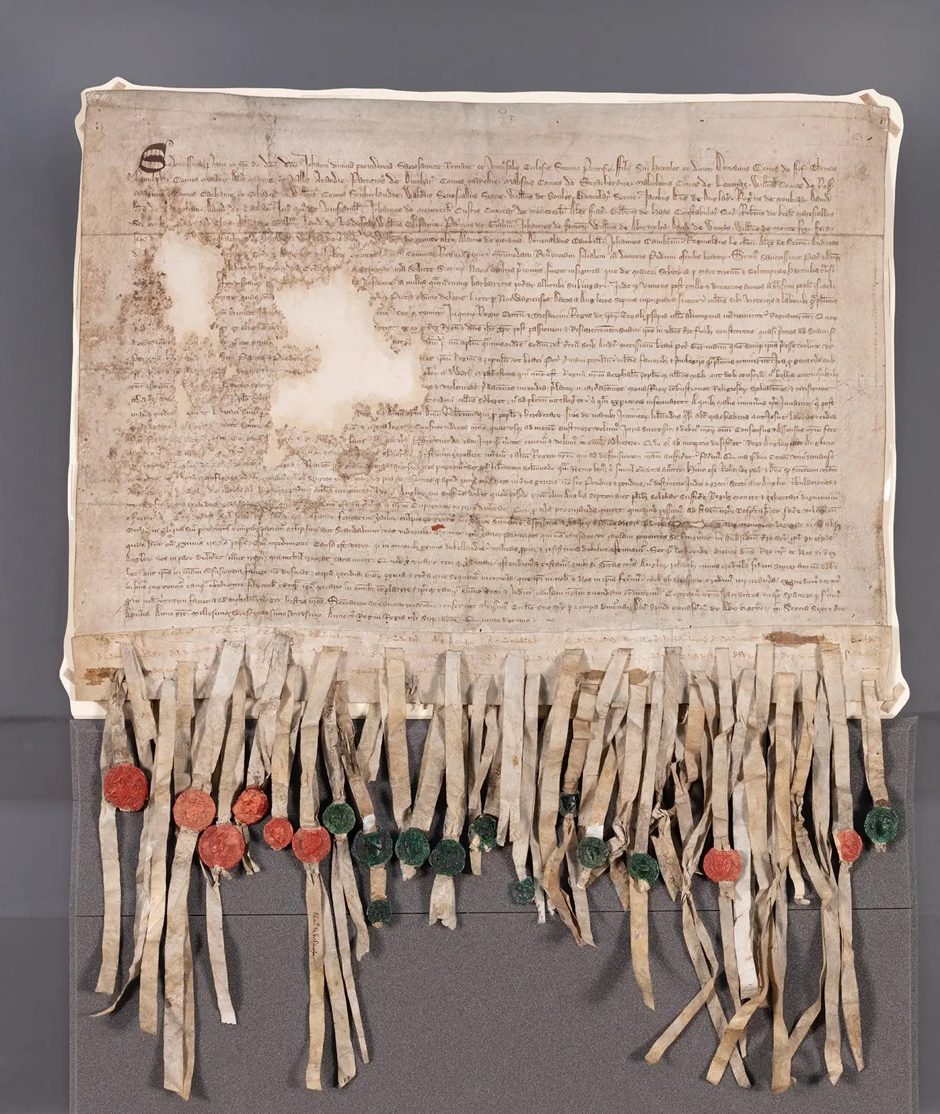 Archival photograph of the original Declaration of Arbroath manuscript, showing stained parchment, lines of Latin handwriting, and pendant seals.