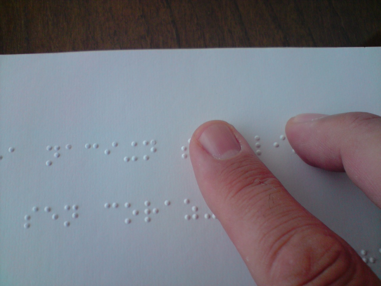 Photograph of a person reading a braille book with two fingers.