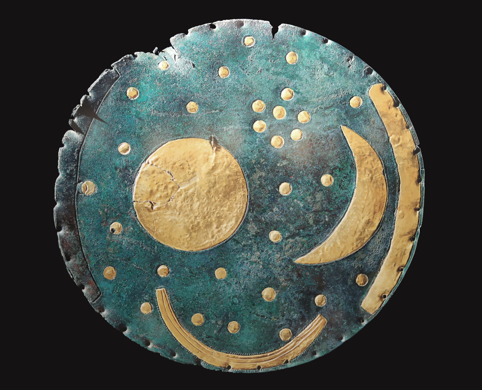Photograph of the Nebra Sky Disc, a green-patinated bronze disc with gold celestial symbols against a dark background.