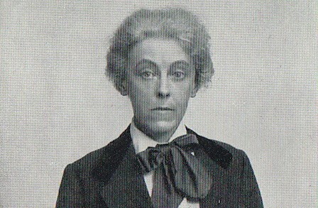 Archival photographic portrait of Charlotte Mew seated in profile beside a table.