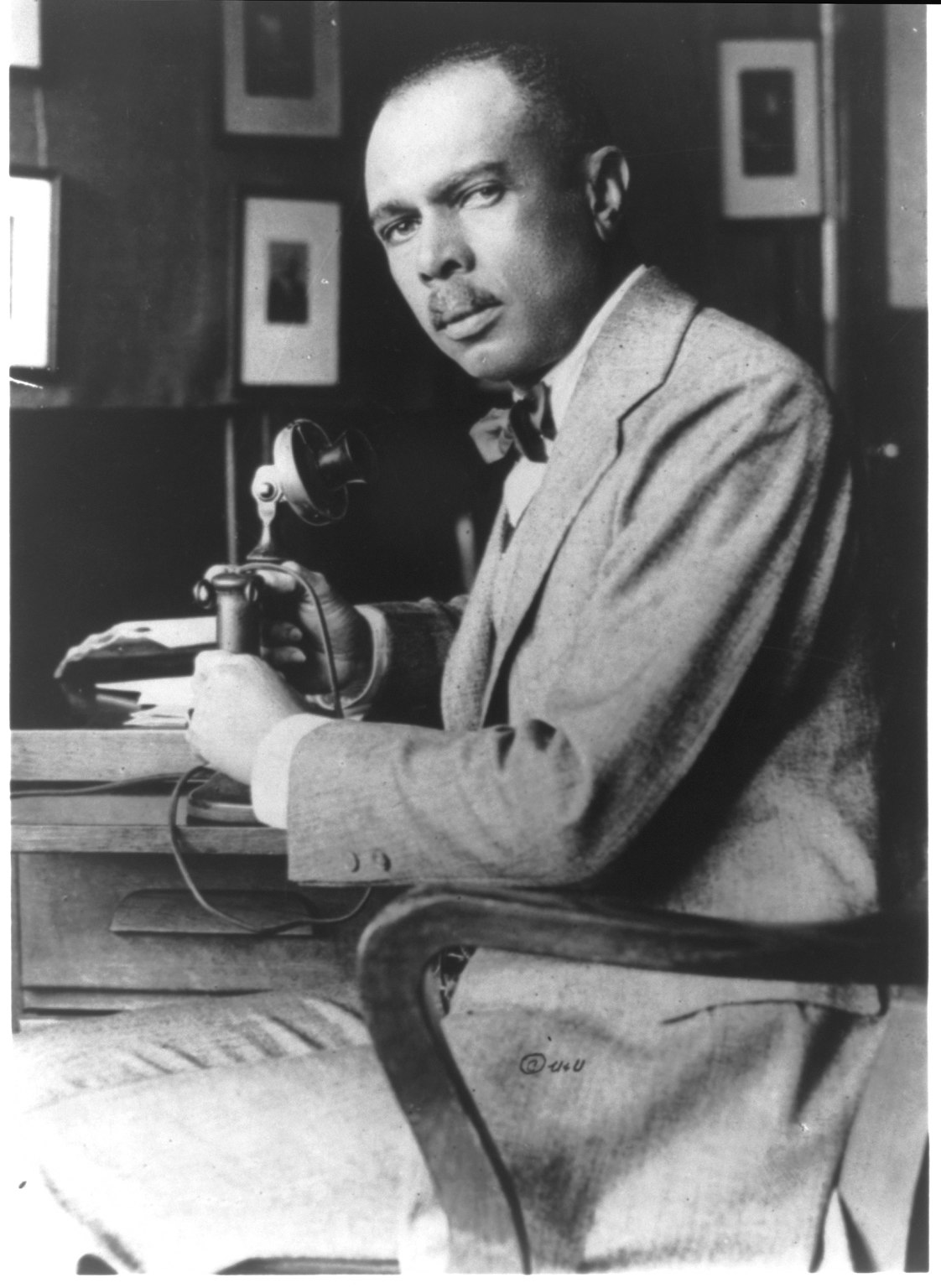 Archival 1900 photographic portrait of James Weldon Johnson seated at a desk with a telephone.