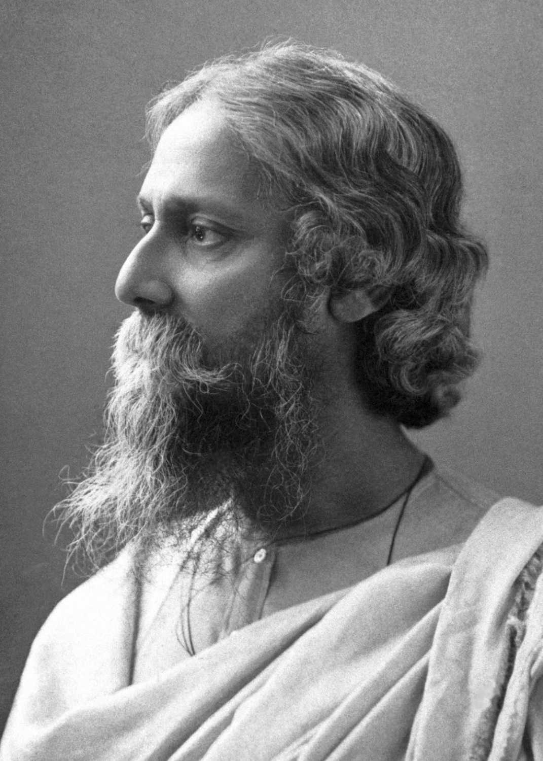 Archival photographic portrait of Rabindranath Tagore in 1909, seated with a long beard and wearing a dark robe.