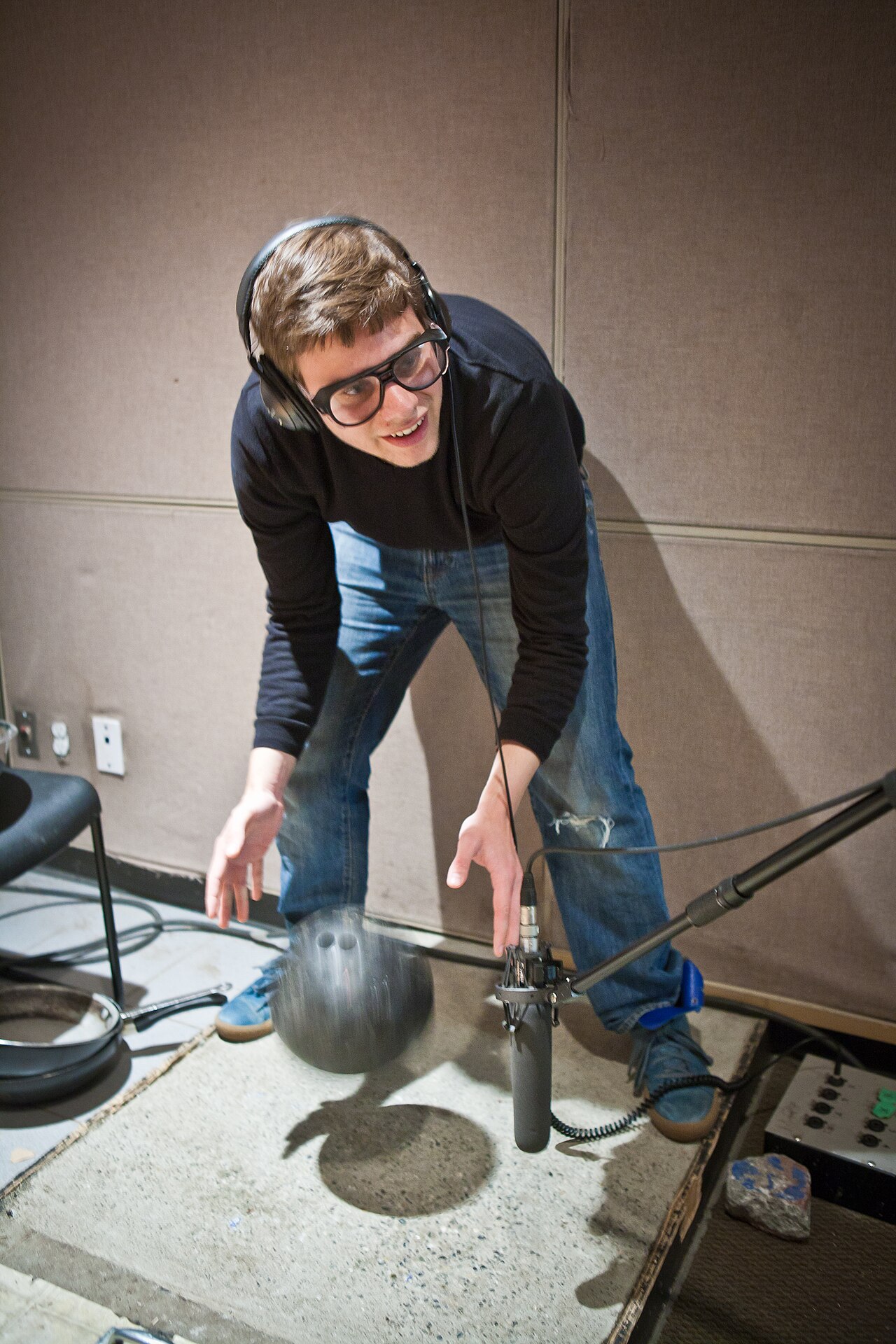 一位戴着耳机的 Foley 艺术家在录音室麦克风旁表演保龄球声音。