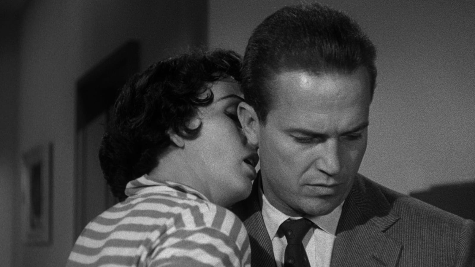 Black-and-white still from Kiss Me Deadly showing Ralph Meeker as Mike Hammer with a woman leaning close beside his face.