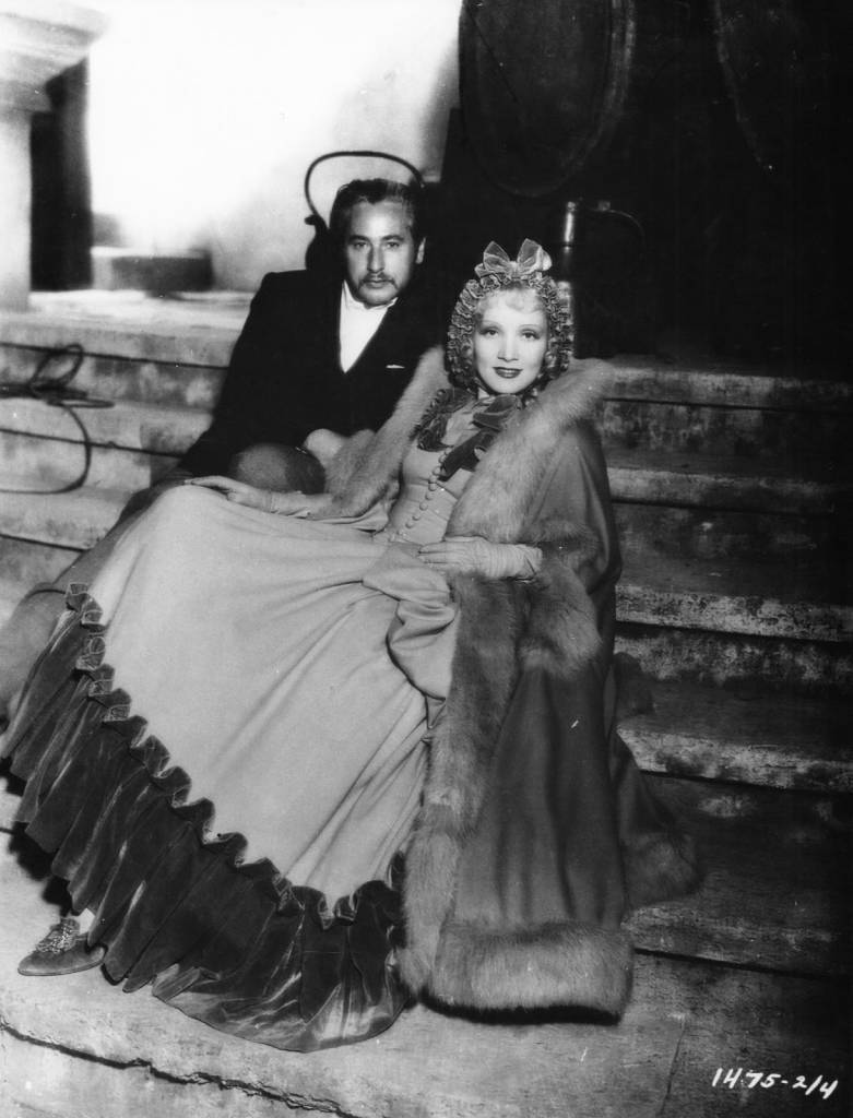 Josef von Sternberg 站在片场，身旁是身着 Sophia 公主戏服的 Marlene Dietrich，出自 1934 年电影 The Scarlet Empress。