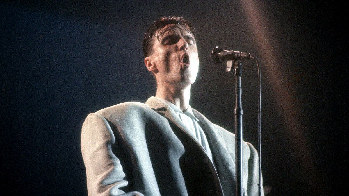 David Byrne sings into a microphone in the oversized pale suit from Stop Making Sense.