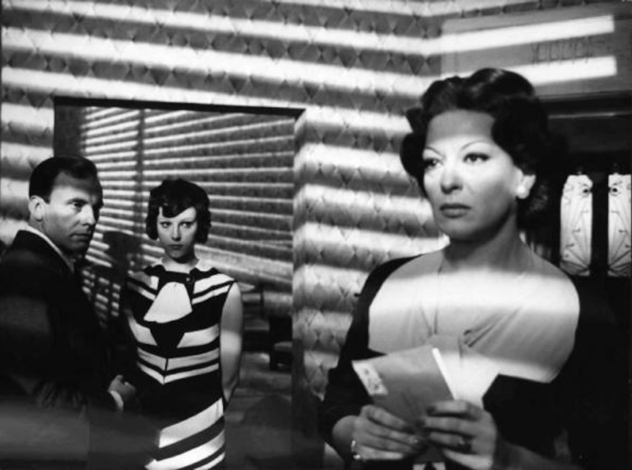A black-and-white archival still from The Conformist showing Jean-Louis Trintignant, Stefania Sandrelli, and Yvonne Sanson inside a patterned modern interior.