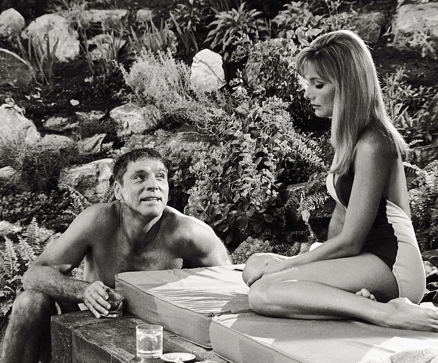 Burt Lancaster crouches beside Janet Landgard in a scene from The Swimmer.