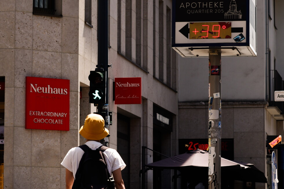 A pedestrian walks below a pharmacy temperature display reading 39 degrees Celsius during Europe's late-June heatwave.
