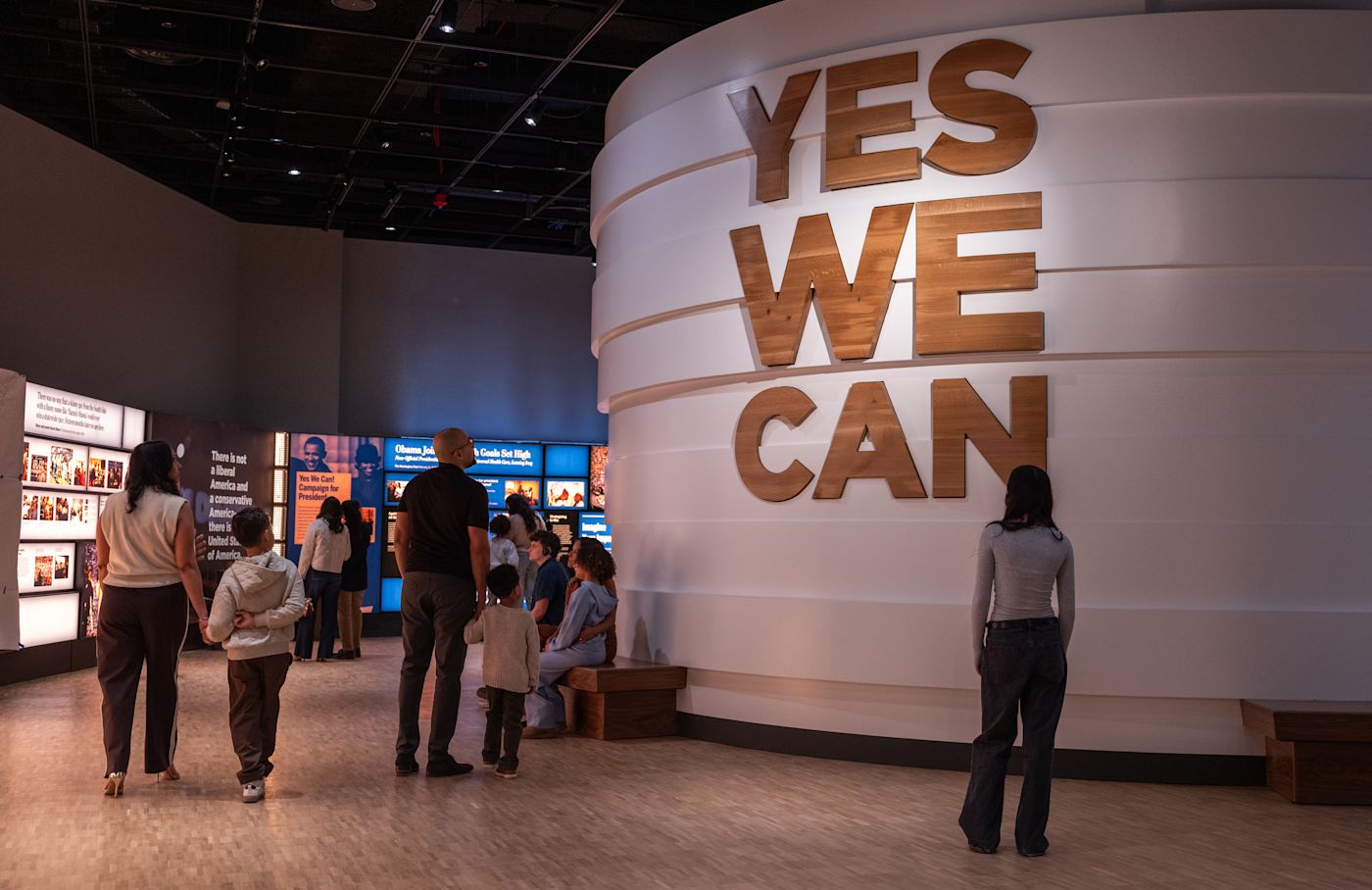 Visitors stand inside the Obama Presidential Center museum near large wood letters reading Yes We Can.