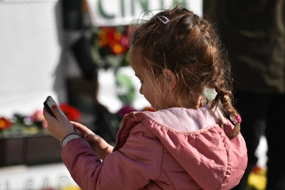 Photograph of a young girl outdoors looking down at a smartphone in her hands.