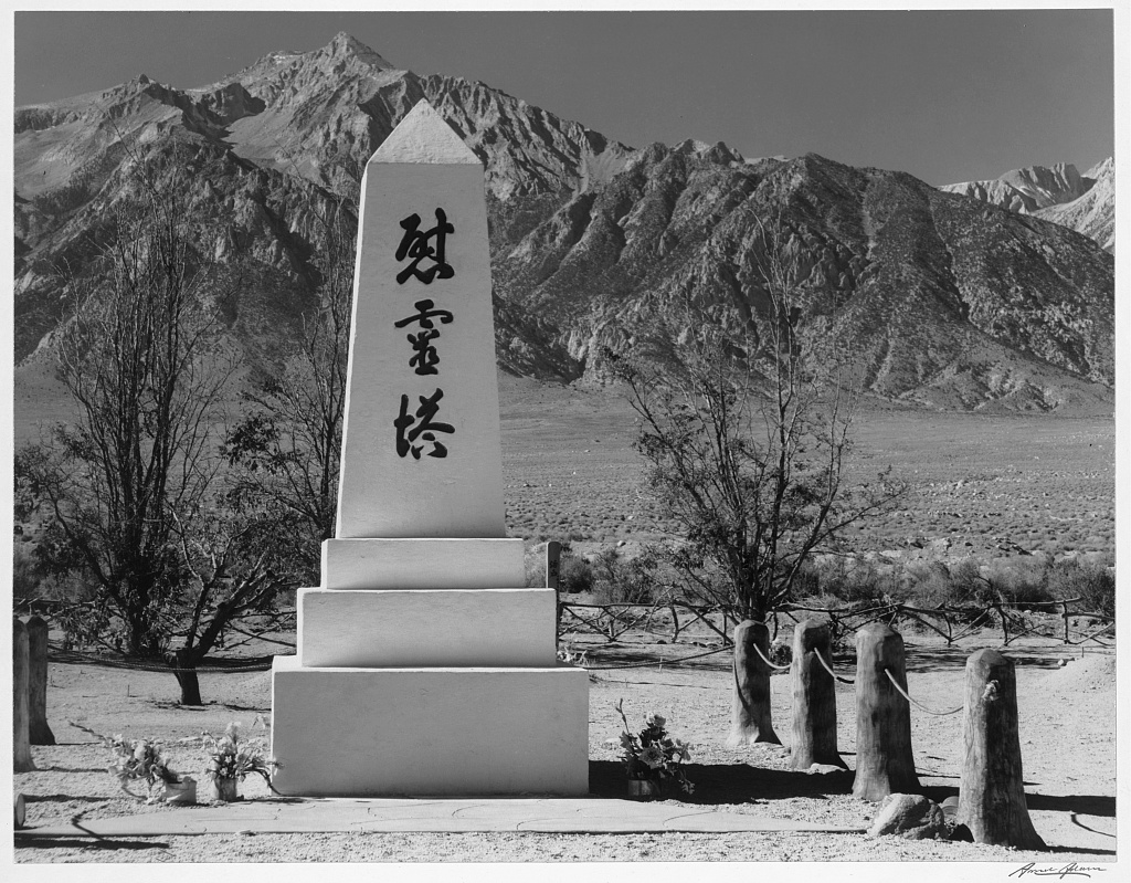 Ansel Adams photograph of the white cemetery monument at Manzanar with mountains behind it.