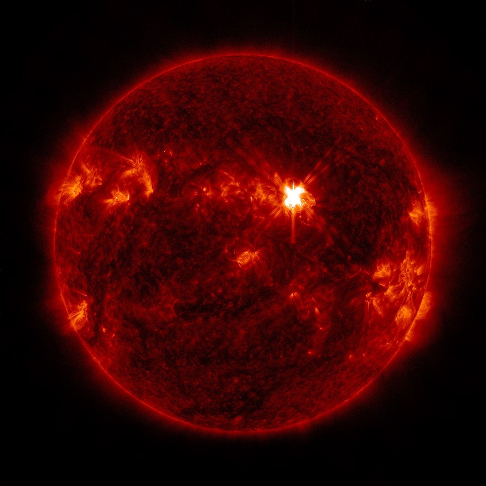 NASA Solar Dynamics Observatory image of a bright solar flare on the red Sun against black space.