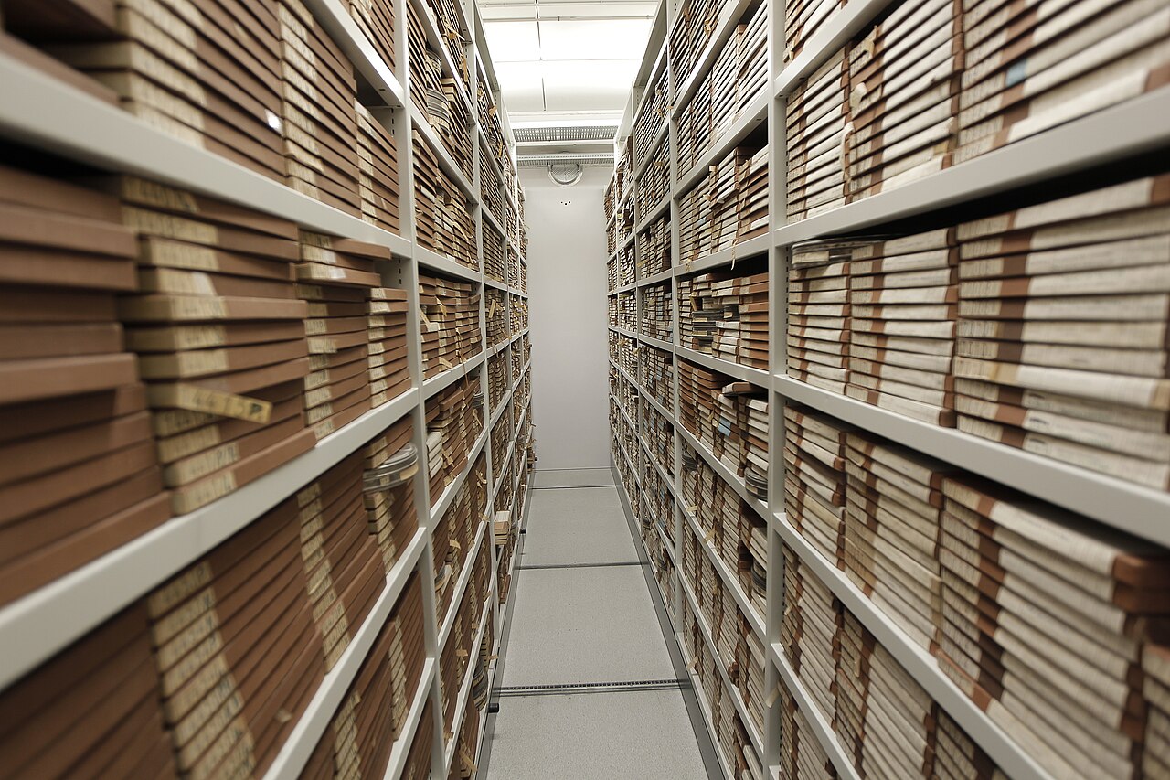 Rows of archival film boxes stored on tall shelves in a Danish Broadcasting Corporation archive aisle.