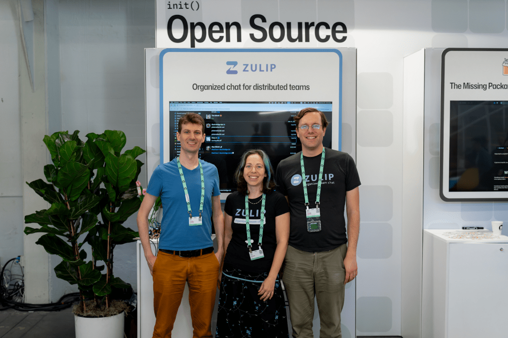 Three Zulip maintainers standing at the Zulip booth in the GitHub Universe 2025 Open Source Zone.
