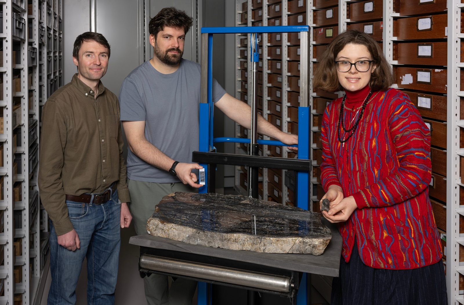 Researchers stand in a paleontology collection room with a large Prototaxites fossil specimen on a work table.