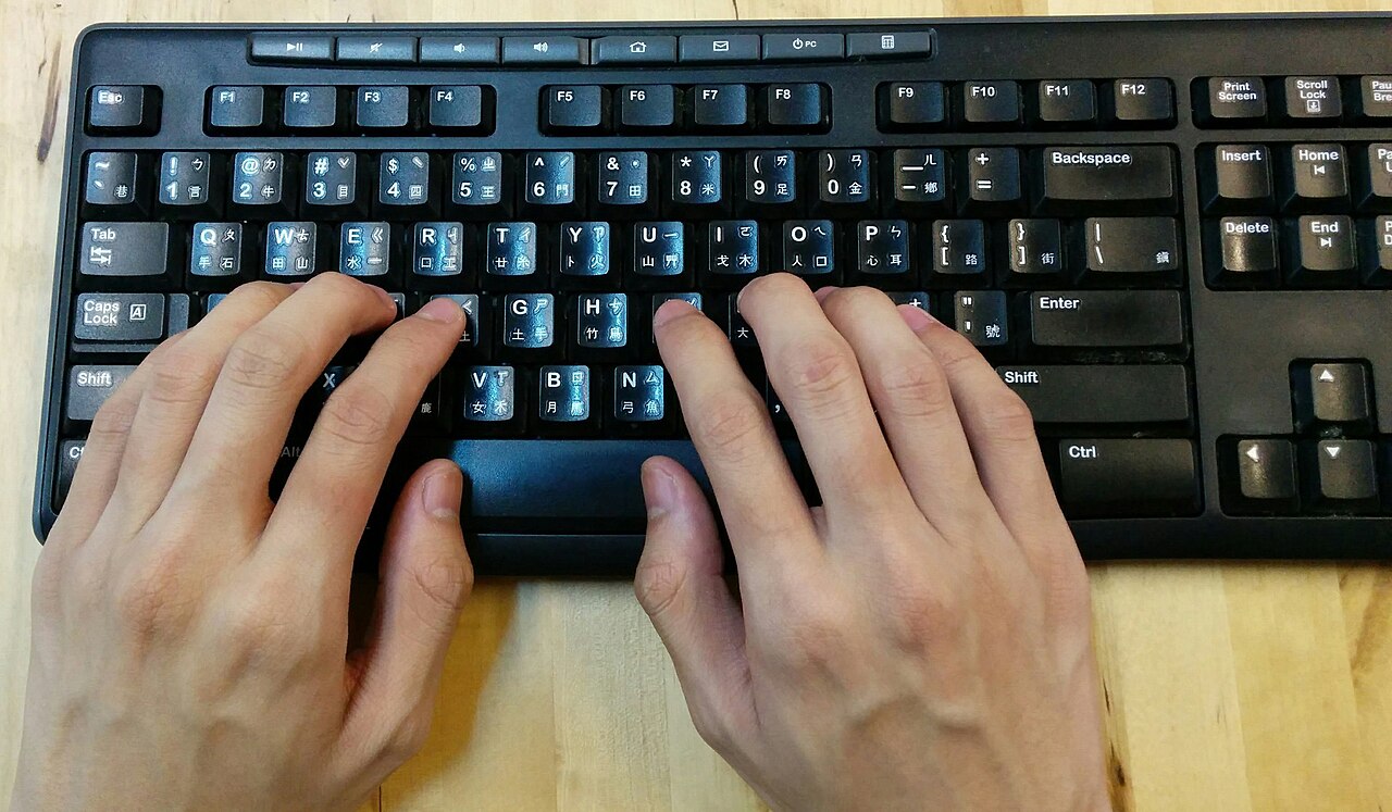 Hands typing on a black keyboard labeled with Latin letters and Chinese input-method symbols.