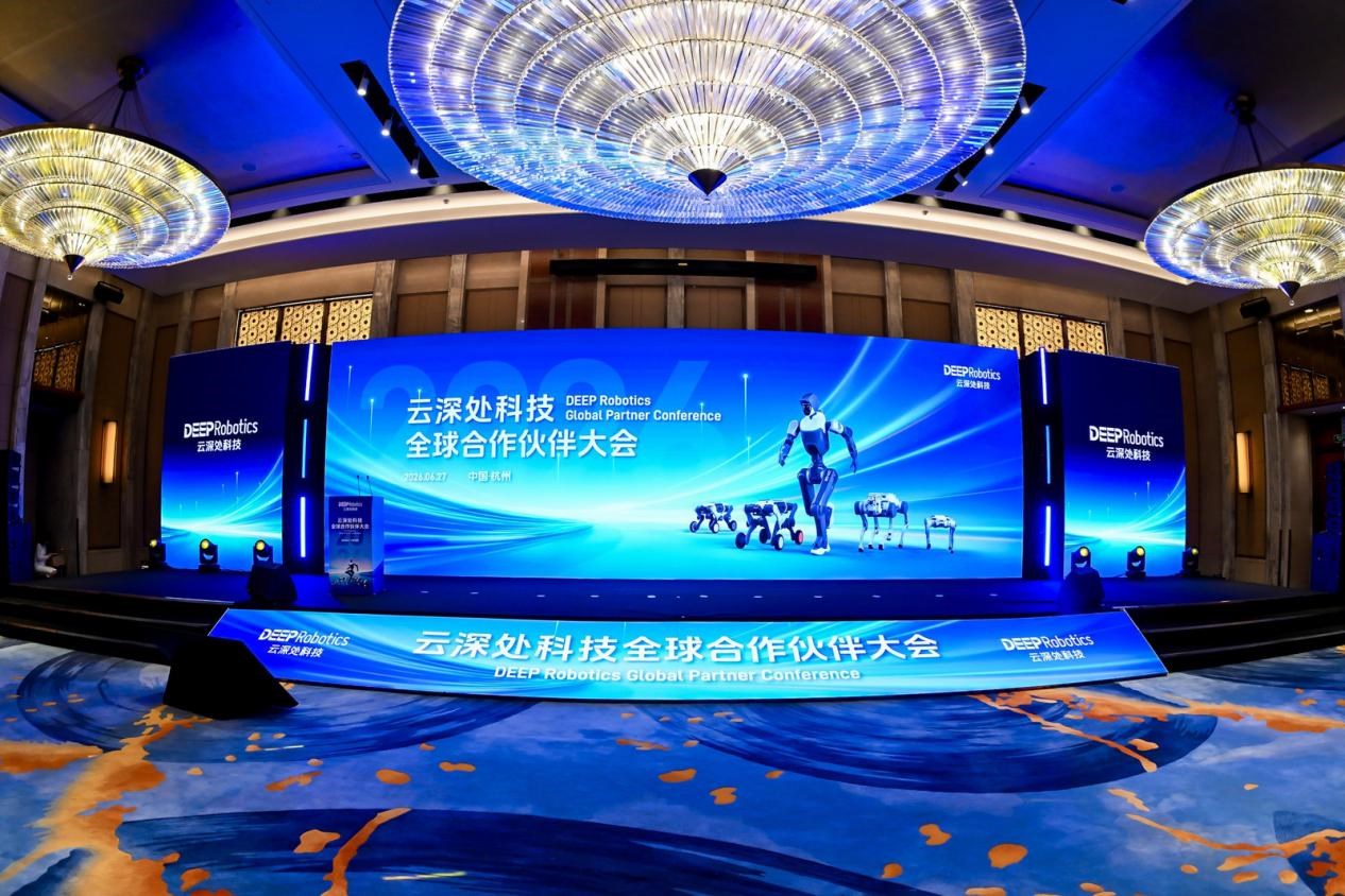 杭州 DEEP Robotics 全球合作伙伴大会舞台的宽幅照片，画面中有大型蓝色屏幕、会议标识和机器人产品图像。