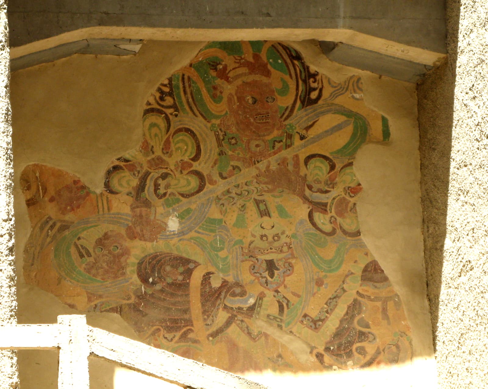A weathered guardian mural stands exposed in the cliff face between Mogao Caves 305 and 306 at Dunhuang.