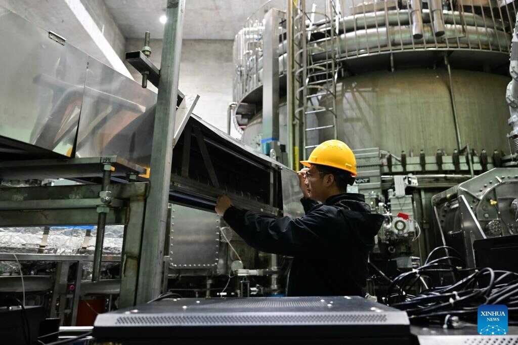 EAST researcher Guo Jin, wearing a yellow hard hat, adjusts equipment inside the metal-lined tokamak hall in Hefei.