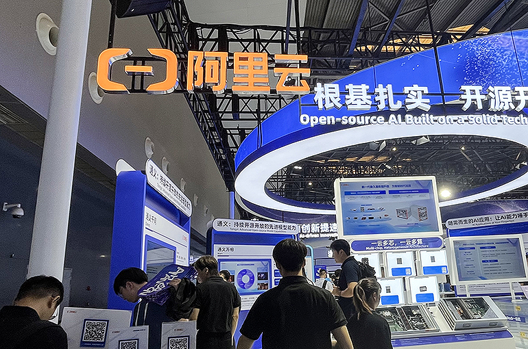 参观者站在一个宣传开源 AI 的阿里云展牌下方，现场是一场科技展会。