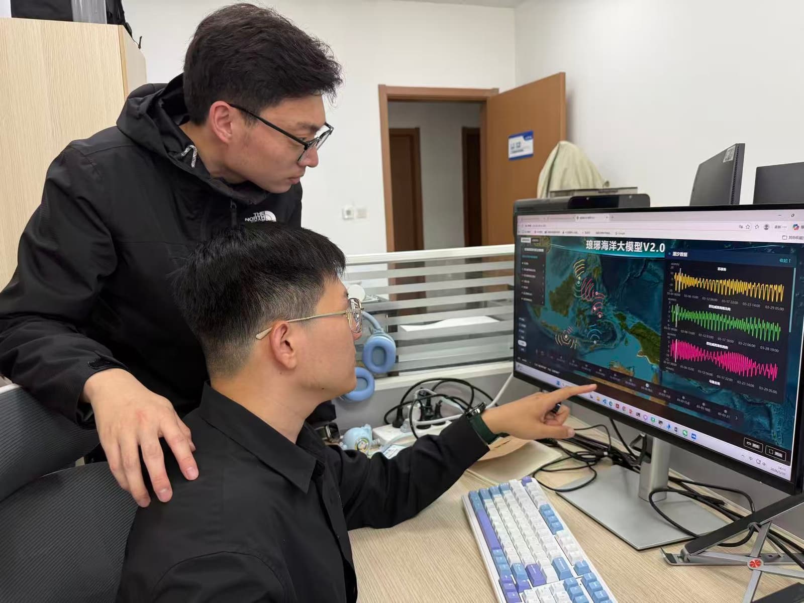 Two members of the Institute of Oceanology research team analyze LangYa model data on a desktop monitor.