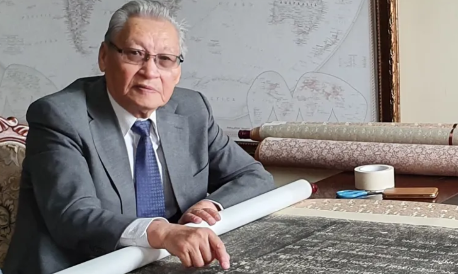 Academician D. Tömörtogoo seated at a table, pointing to lines of vertical Mongolian script on an archival manuscript.