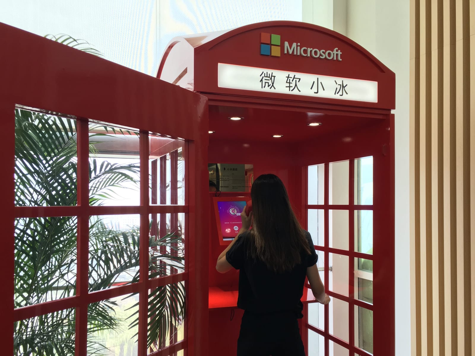 A visitor stands inside a red Microsoft XiaoIce demonstration booth and uses its touchscreen.