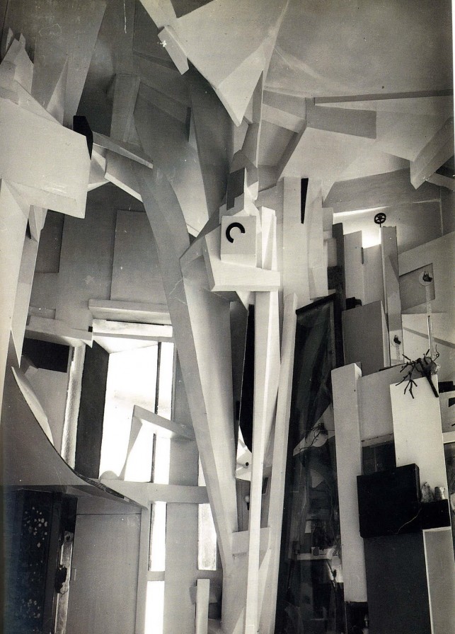 Wilhelm Redemann's 1933 black-and-white photograph of Kurt Schwitters's Hanover Merzbau, showing angular white plaster forms, columns, cavities, and found-object details filling an interior room.